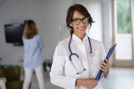 Foto de Doctora que usa bata de laboratorio y estetoscopio y sostiene el portapapeles en sus manos mientras está parada en el pasillo del hospital - Imagen libre de derechos