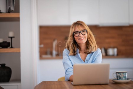 Photo for Beautiful mid aged woman using laptop while working from home. Home office. - Royalty Free Image