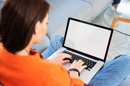 Foto de Rear view of  woman sitting at home and using laptop. Empty screen. - Imagen libre de derechos