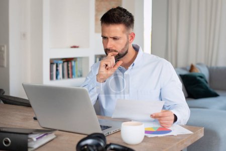 Téléchargez les photos : Thinking businessman sitting at desk at home using laptop for work. Home office. - en image libre de droit
