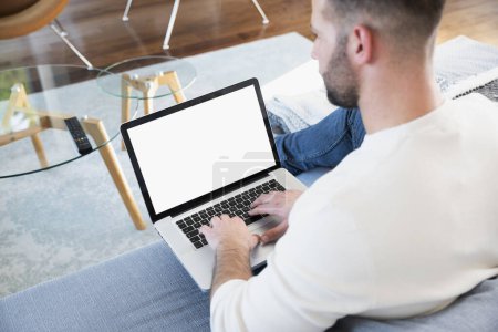 Photo for Rear view shot of man wearing casual clothes and relaxing on the sofa while working from home. Confident man using laptop for work. - Royalty Free Image