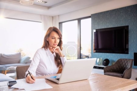 Foto de Thinking mid aged woman sitting at home and using laptop for work. Confident businesswoman working from home Home office. - Imagen libre de derechos