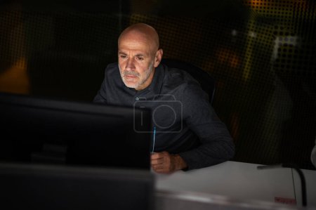 Foto de Tiro de serio hombre de negocios reflexivo sentado en la mesa con el ordenador en la oficina en la tarde. - Imagen libre de derechos