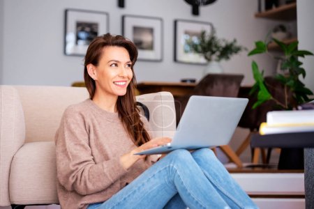 Photo for Shot of an attractive middle aged woman sitting at home and using laptop. Beautiful female wearing casual clothes. - Royalty Free Image