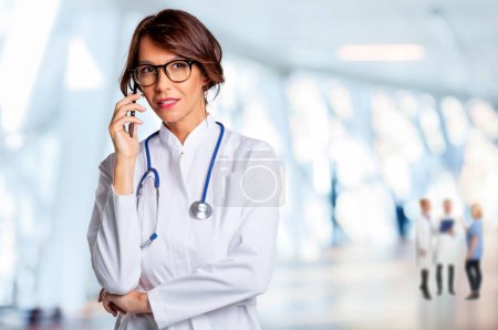 Téléchargez les photos : Portrait d'une femme médecin souriante utilisant un téléphone portable et parlant avec sa patiente à la clinique. Un travailleur de la santé confiant porte une blouse de laboratoire. - en image libre de droit