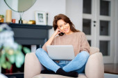 Shot of an attractive middle aged woman sitting in an armchair while using laptop and having video call. Beautiful female wearing casual clothes. Poster #644556478
