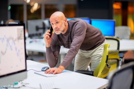 Foto de Pensando en un hombre de negocios de mediana edad parado en el escritorio de la oficina y usando la computadora - Imagen libre de derechos