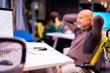 Téléchargez les photos : Pensant homme d'affaires d'âge moyen debout au bureau et en utilisant l'ordinateur - en image libre de droit