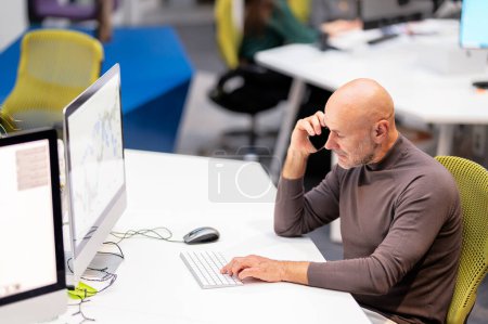 Foto de Pensando en un hombre de negocios sentado en el escritorio de la oficina y trabajando en el teléfono y la computadora. Mide anciano profesional hombre teniendo una llamada de negocios. - Imagen libre de derechos