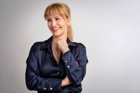 Photo for Close-up of an attractive middle aged woman smiling and looking away. Blond haired female wearing casual clothes while standing at isolated white background. Copy space. Studio shot. - Royalty Free Image