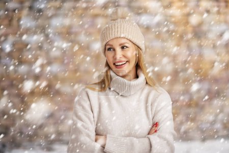 Foto de Hermosa mujer sonriente divirtiéndose en la nieve. Mujer rubia con sombrero de punto y suéter de cuello alto. Copiar espacio. - Imagen libre de derechos