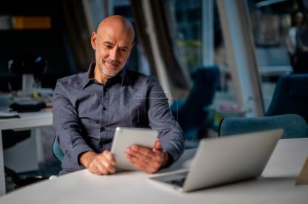 Téléchargez les photos : Homme d'affaires utilisant tablette numérique et pavé tactile tout en étant assis dans un bureau moderne. - en image libre de droit