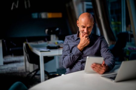 Téléchargez les photos : Homme d'affaires utilisant la tablette et le pavé tactile diigital tout en étant assis dans un bureau moderne. Multitâche. - en image libre de droit