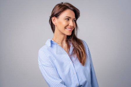Photo for Smiling brunette businesswoman standing against grey background. Confident female professional is wearing blue shirt. She is having brown hair. Copy space. - Royalty Free Image