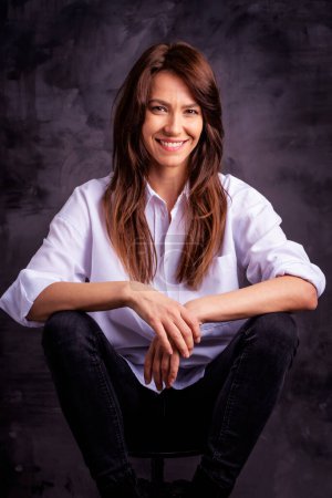 Foto de Atractiva mujer de mediana edad con sonrisa dentada con camisa blanca y jeans negros - Imagen libre de derechos