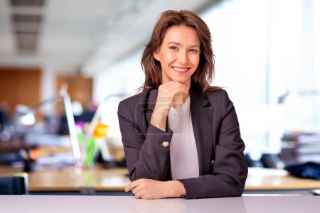 Foto de Portait de una atractiva mujer de negocios vestida de chaqueta negra mientras estaba sentada en la oficina. Copiar espacio. Mano en la barbilla. - Imagen libre de derechos