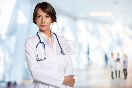 Photo for Smiling female doctor wearing lab coat and stethoscope and standing at the hospital corridor. - Royalty Free Image