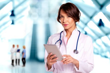 Téléchargez les photos : Portrait d'une femme médecin tenant sa tablette numérique debout dans le couloir de l'hôpital. - en image libre de droit