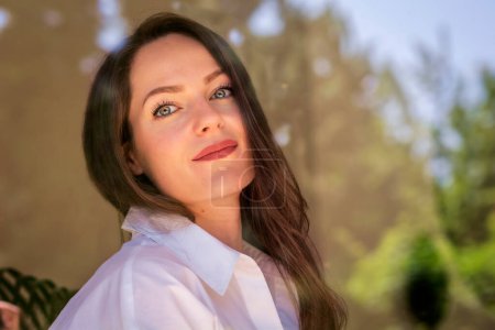 Photo for Headshot of beautiful young woman standing behind the glass window and looking at camera. Attractive female having blue eyes and brunette long hair. - Royalty Free Image