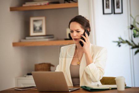 Foto de Mujer preocupada sentada en casa y trabajando. Mujer de negocios usando computadoras portátiles y haciendo una llamada. Oficina en casa. - Imagen libre de derechos