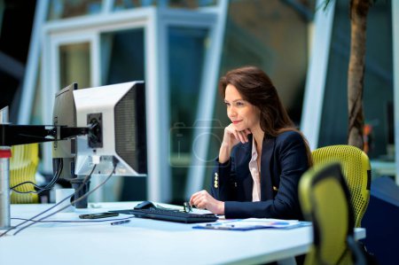 Foto de Mujer de mediana edad que usa computadoras mientras está sentada en el escritorio de la oficina. Mujer profesional que trabaja en un nuevo proyecto empresarial. - Imagen libre de derechos