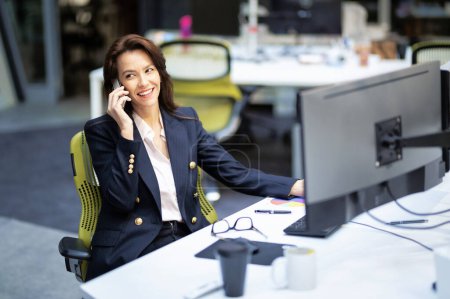 Téléchargez les photos : Femme d'affaires d'âge moyen utilisant des ordinateurs et ayant un appel téléphonique tout en étant assis au bureau au bureau. Femme professionnelle travaillant sur un nouveau projet d'entreprise. - en image libre de droit