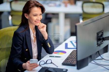 Photo for Middle aged business woman using computers while sitting at desk at the office. Professional female working on new business project. - Royalty Free Image