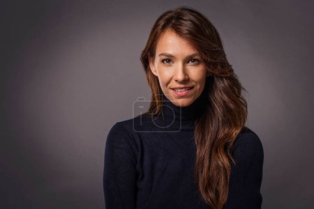 Photo for Studio portrait of a beautiful middle-aged woman looking at the camera. Close-up of an attractive long haired female wearing black sweater and cheerful smiling. - Royalty Free Image