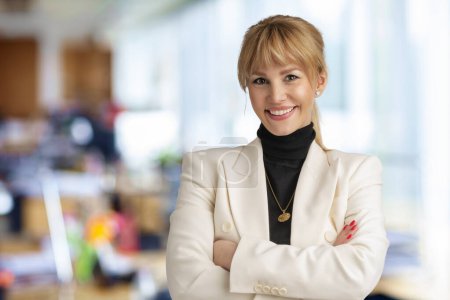 Photo for Close-up of confident businesswoman wearing blazer and standing at the office. Blond haired professional woman looking at camera and cheerful smiling. - Royalty Free Image