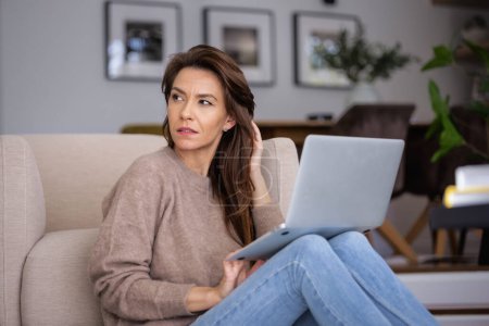 Photo for Portrait of beautiful long haired woman wearing casual clothes while using laptop for work at home. Confident female sitting on the floor and having video call. - Royalty Free Image