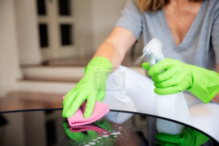 Großaufnahme der Hand einer Frau, die zu Hause den Couchtisch wischt. Selbstbewusste Frau mit Gummihandschuhen und Reinigungsflüssigkeit.