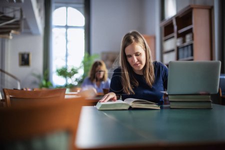 Téléchargez les photos : Une jeune femme malvoyante assise et étudiant à la bibliothèque universitaire. Jeune femme utilisant un ordinateur portable et des livres. - en image libre de droit