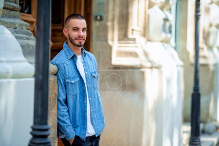Photo for Close-up portrait of a stylish young man standing in the doorway in a city street. Young male looking at camera and wearing casual clothes. - Royalty Free Image