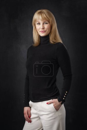 Photo for Beautiful smiling woman standing at isolated dark background. Blond haired woman wearing black turtleneck sweater. Copy space. - Royalty Free Image