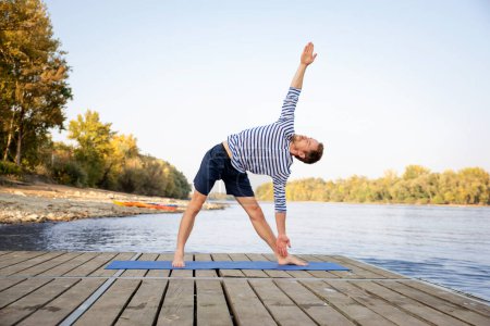 Photo for Mid aged man practicing yoga outdoor. Caucasian man using yoga mat and doing yoga on nature. - Royalty Free Image