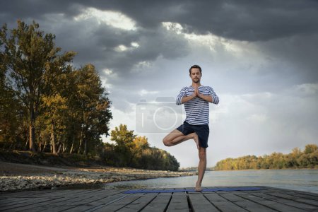 Foto de Hombre de mediana edad practicando yoga al aire libre y de pie equilibrio yoga pose. - Imagen libre de derechos