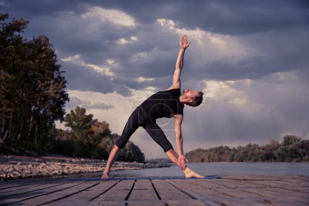 Foto de Hombre practicando yoga al aire libre. Hombre caucásico usando esterilla de yoga y estiramiento. - Imagen libre de derechos