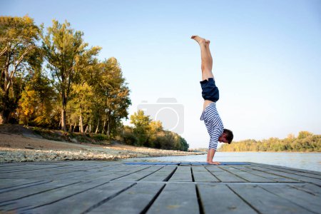 Foto de Hombre practicando yoga al aire libre. Hombre caucásico usando esterilla de yoga y haciendo yoga en la naturaleza. Soporte de mano de yoga. - Imagen libre de derechos