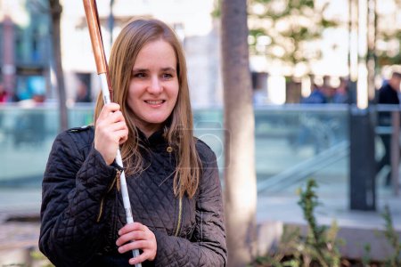 Photo for Close-up of a visually impaired woman holding a white cane and sitting on a bench in the city - Royalty Free Image