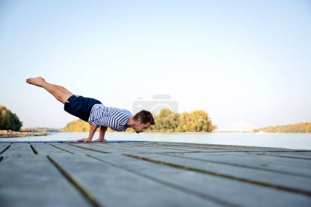 Téléchargez les photos : Homme d'âge moyen pratiquant le yoga en plein air. Homme caucasien utilisant tapis de yoga et faire du yoga à la nature. Poignées de yoga. - en image libre de droit