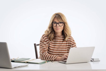 Foto de Mujer de negocios de pelo rubio sentada en el escritorio y trabajando en computadoras portátiles sobre un fondo aislado. Copiar espacio. - Imagen libre de derechos
