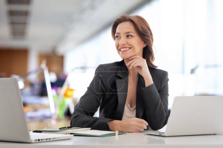 Téléchargez les photos : Femme d'affaires assise au bureau. Femme professionnelle confiante utilisant des ordinateurs portables pour les travaux. Espace de copie. - en image libre de droit
