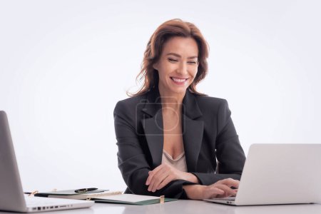 Photo for Mid age businesswoman sitting at desk against isolated background. Confident professional female using laptops for work. Copy space. - Royalty Free Image
