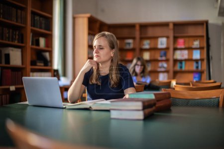Photo for A visually impaired woman sitting and studying in the university library. Young  woman  using laptop and books. - Royalty Free Image
