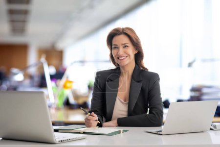 Foto de Morena mujer de negocios de pelo sentado en la oficina y el uso de computadoras portátiles para el trabajo. Mujer profesional de confianza que usa chaqueta. - Imagen libre de derechos