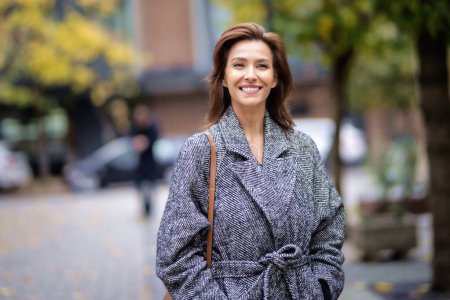 Photo for Portrait of a middle adult woman with brunette hair walking outdoors in city street on autumn day. She is wearing tweed coat. - Royalty Free Image
