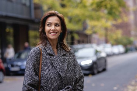 Photo for Portrait of a middle adult woman with brunette hair walking outdoors in city street on autumn day. She is wearing tweed coat. - Royalty Free Image