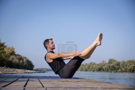Foto de Hombre de mediana edad practicando yoga al aire libre. Caucásico hombre usando yoga mat y haciendo barco pose en la naturaleza. - Imagen libre de derechos