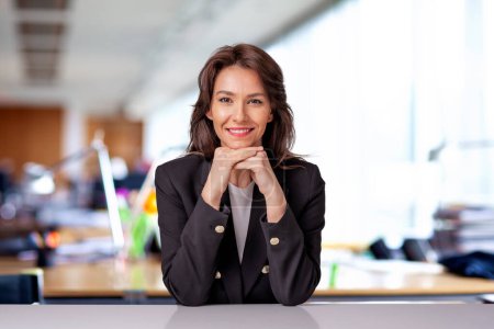Téléchargez les photos : Portrait d'une jolie femme d'affaires portant un blazer noir alors qu'elle était assise au bureau. - en image libre de droit