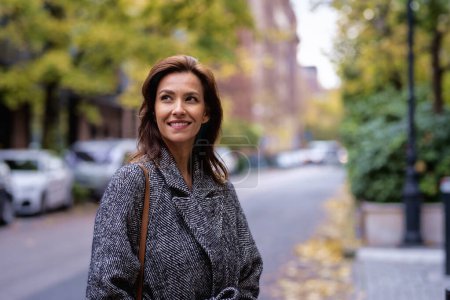 Portrait d'une femme moyenne adulte aux cheveux bruns marchant à l'extérieur dans la rue de la ville le jour de l'automne. Elle porte un manteau en tweed..